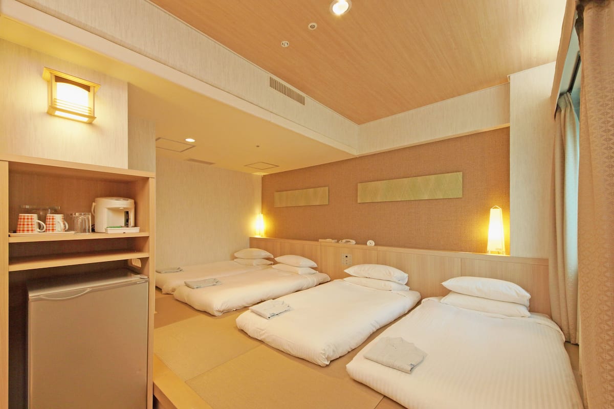 Ein Hotelzimmer mit drei Betten, einer Minibar und einer kleinen Sitzecke.