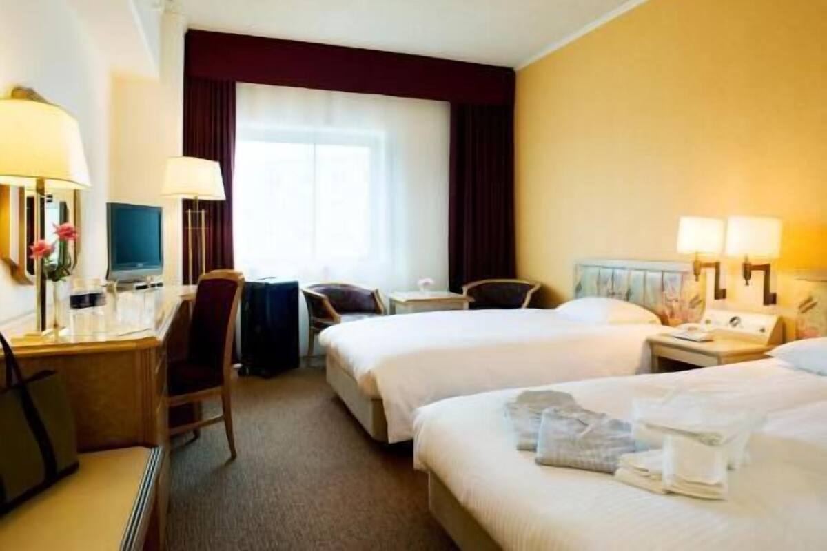 Ein Hotelzimmer mit zwei Betten, einem Schreibtisch, einem Stuhl, einem Fernseher und einem Fenster mit Vorhängen.