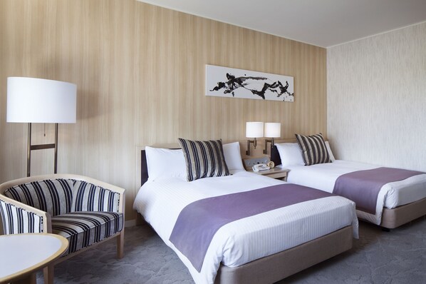 Habitación de hotel con dos camas, una silla, una mesa y una lámpara.
