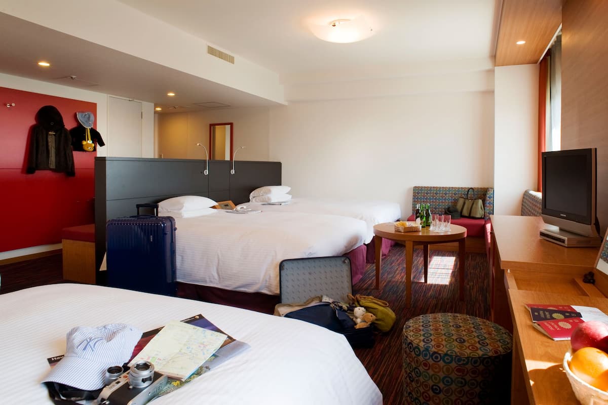 Ein Hotelzimmer mit zwei Betten, einem Schreibtisch mit Computer, einem kleinen Tisch mit Flaschen und einem Fernseher.