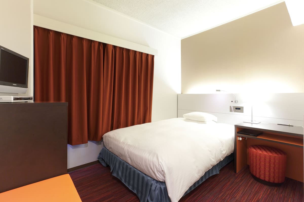 Ein Hotelzimmer mit Bett, Schreibtisch, Fernseher und einem roten Hocker.