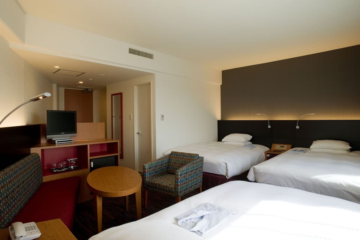 Ein Hotelzimmer mit zwei Betten, einem Fernseher, einem kleinen Tisch, einem Stuhl und einem Schreibtisch mit Telefon.