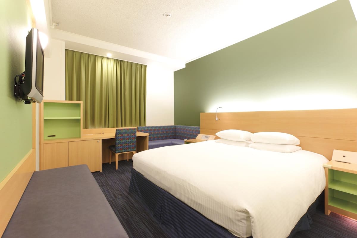 Ein Hotelzimmer mit Bett, Schreibtisch, Stuhl, Fernseher und einem grünen Vorhang.