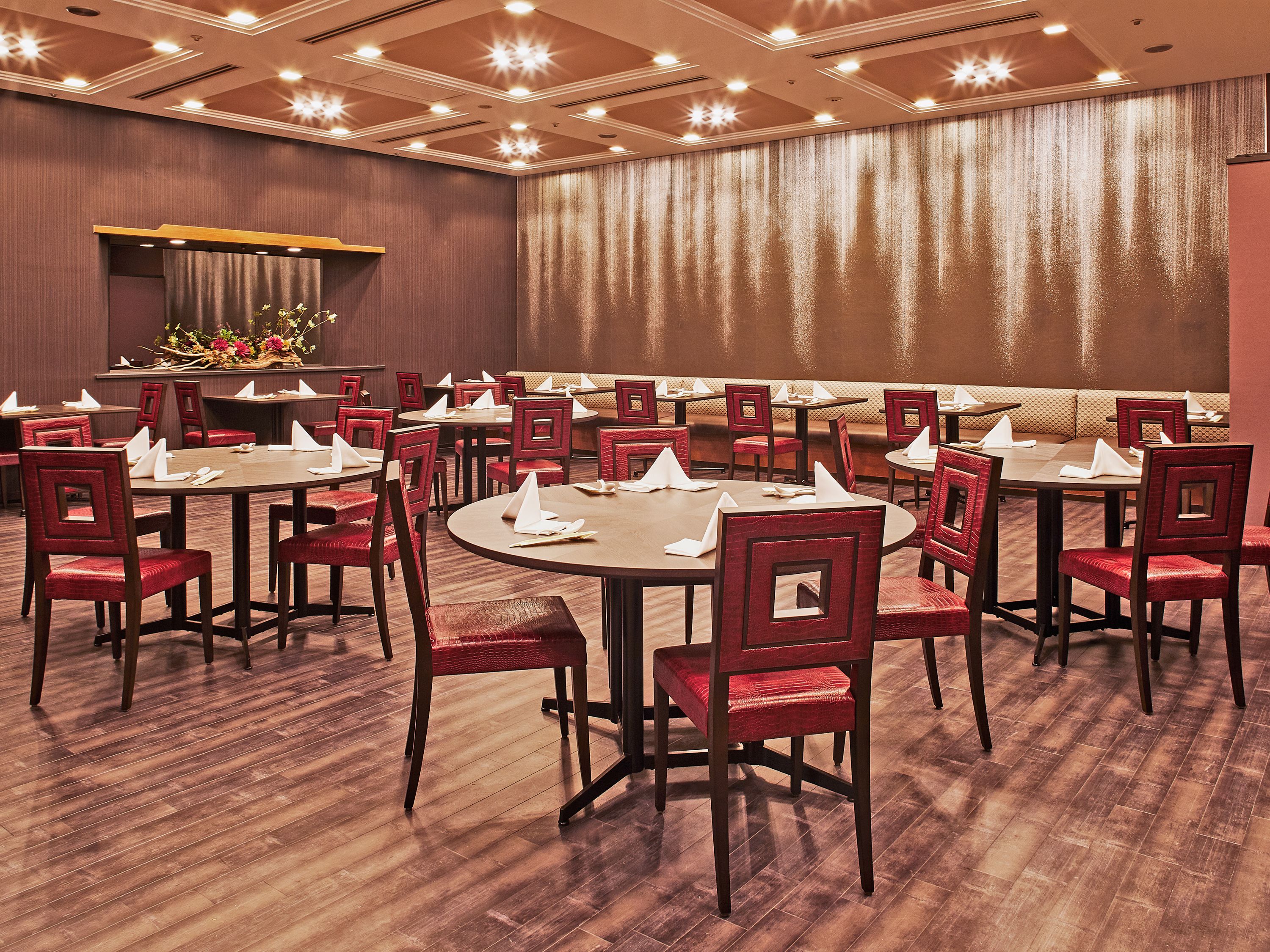 A conference room with round tables and red chairs, equipped with white napkins and menus.