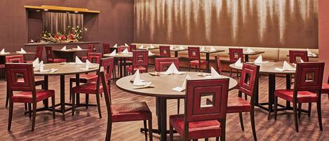 A conference room with round tables and red chairs, equipped with white napkins and menus.