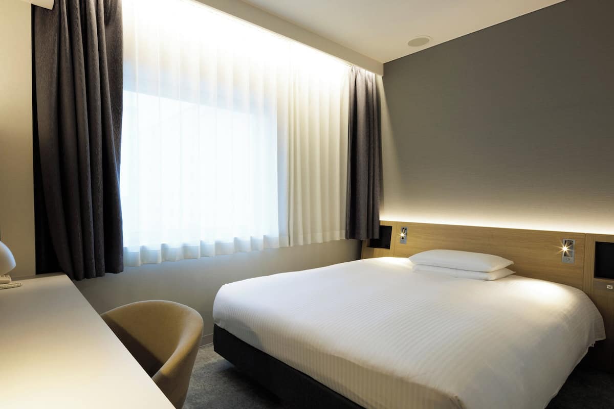 Ein Hotelzimmer mit Bett, Schreibtisch, Stuhl und einem Fenster mit Vorhängen.