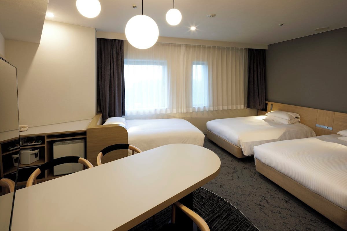 Ein Hotelzimmer mit zwei Betten, einem Schreibtisch, Stühlen, einem kleinen Tisch und einem Fenster mit Vorhängen.