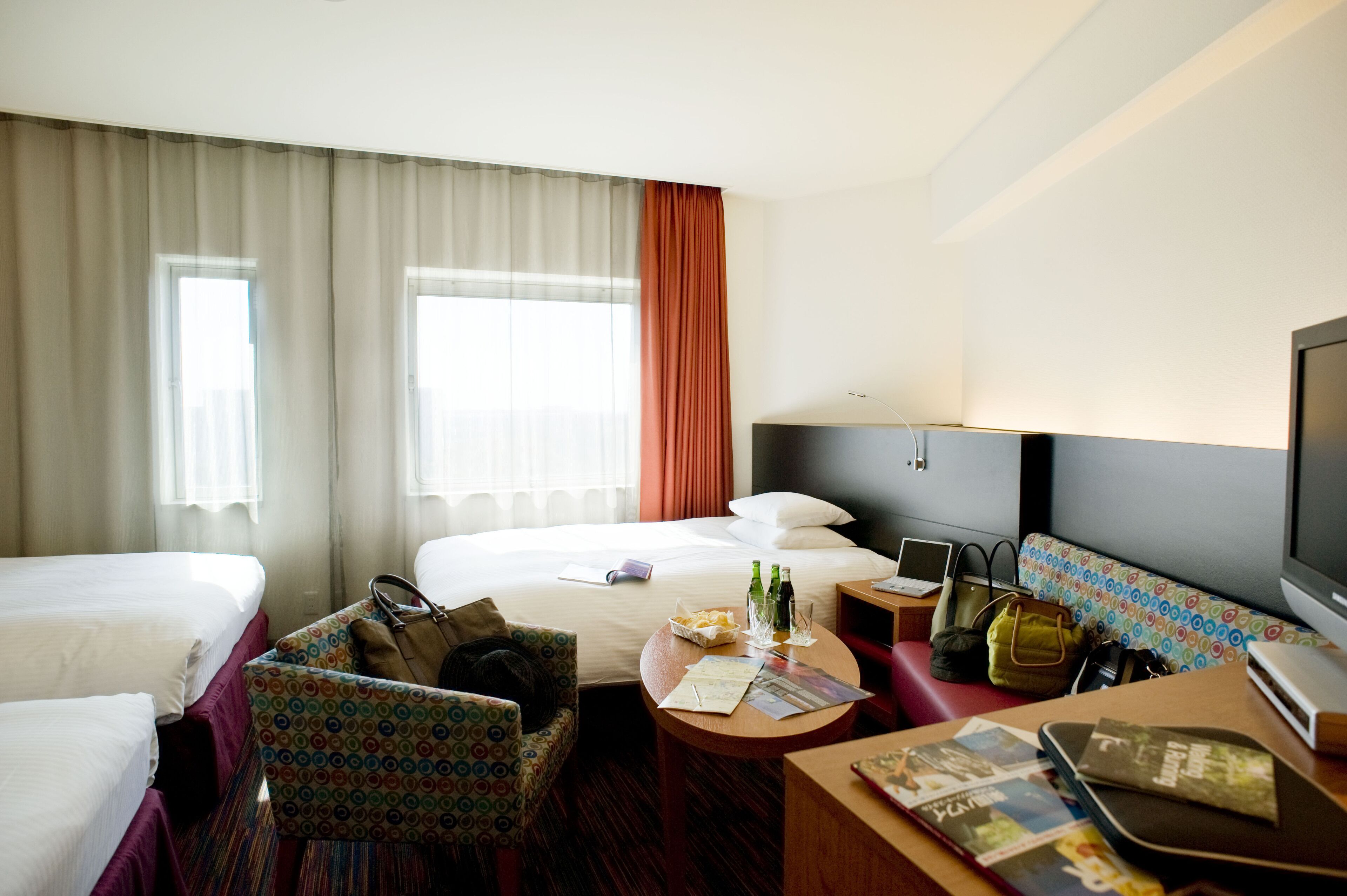 Habitación de hotel con dos camas, un escritorio, una silla, un televisor y una ventana con cortinas.