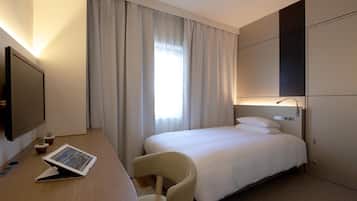 A hotel room with a bed, a desk with a tablet, a chair, a TV, and a window with curtains.