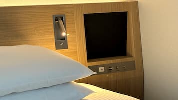 Habitación de hotel con cabecera de madera, panel de control con botones y pantalla, y una cama bien hecha con ropa blanca.