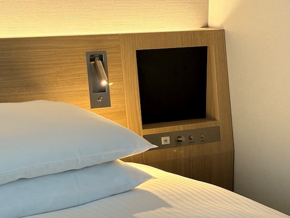 Habitación de hotel con cabecera de madera, panel de control con botones y pantalla, y una cama bien hecha con ropa blanca.