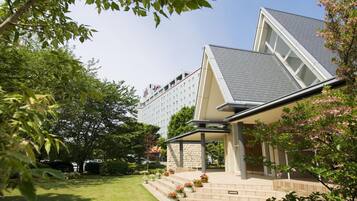 Een hotel met een modern design, met een opvallende glazen gevel en een aangelegde tuin met trappen naar de ingang.