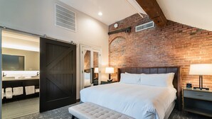 A bedroom with a large bed, a bench, a brick wall, and a bathroom visible through an open door. - Columbus Marriott (Columbus)