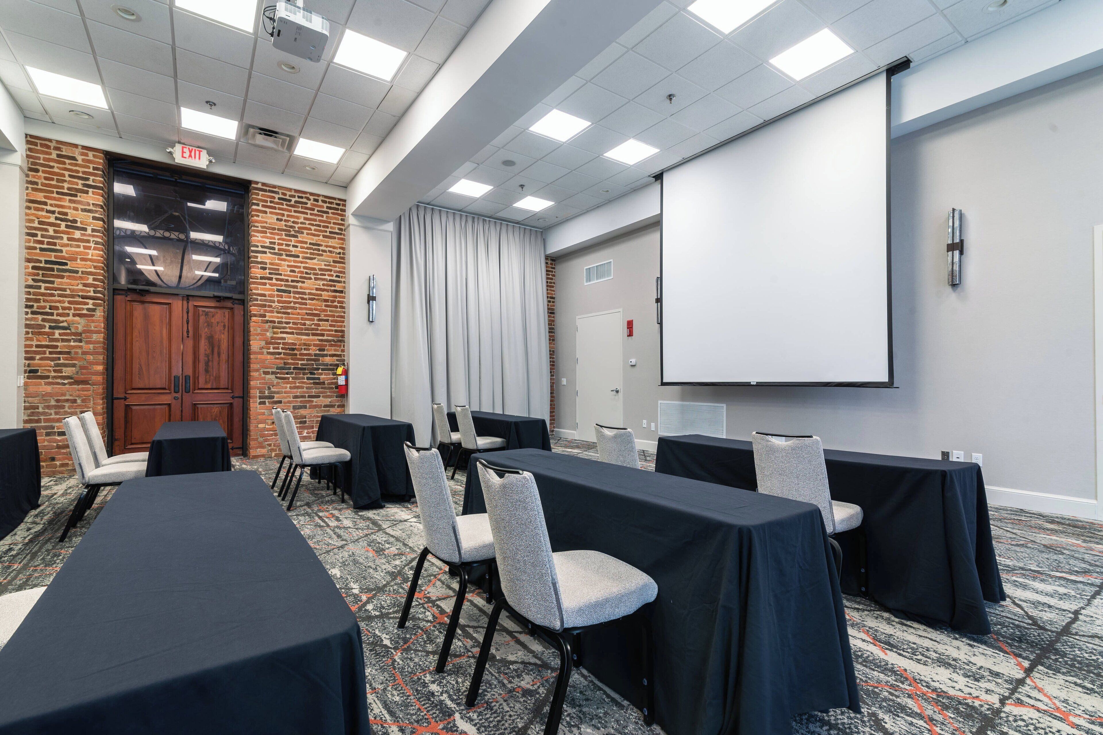 Un salón de conferencias con pared de ladrillo, una pantalla grande y mesas con sillas.