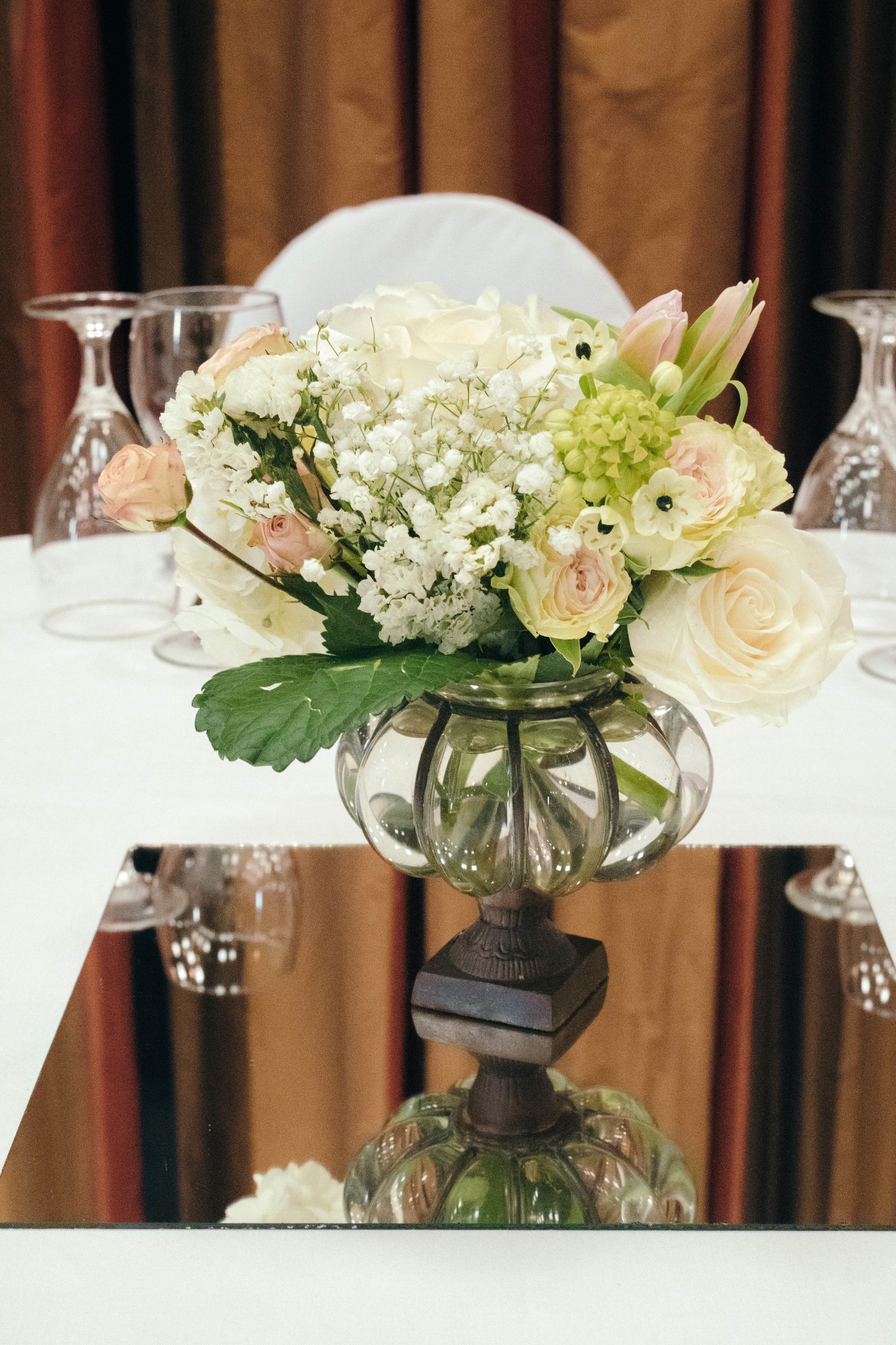 A table with a vase of flowers and wine glasses.