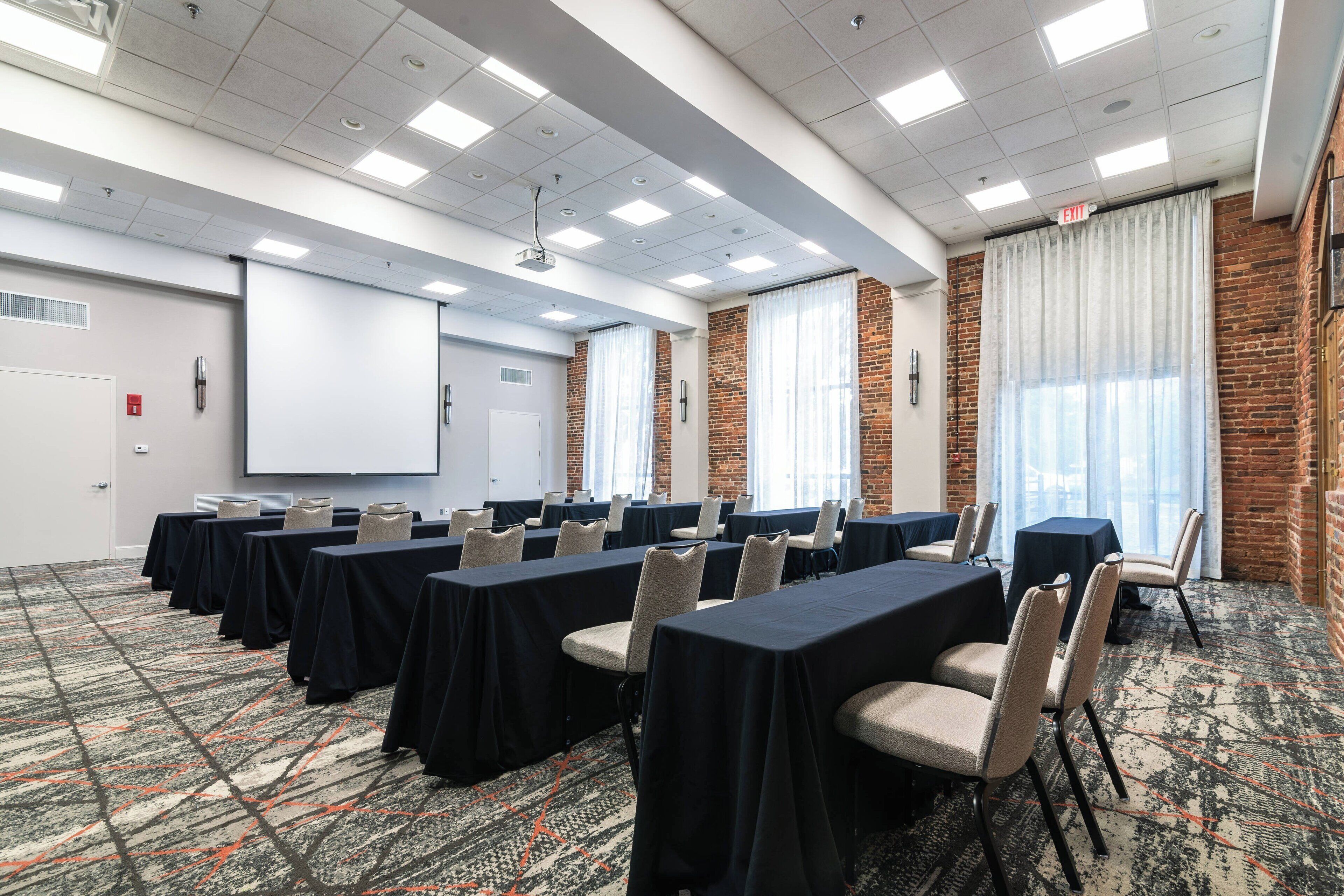 A conference room with tables and chairs, a projector screen, and a brick wall.