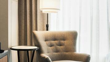 A hotel room with a single armchair, a small round table, a lamp, and a bed.