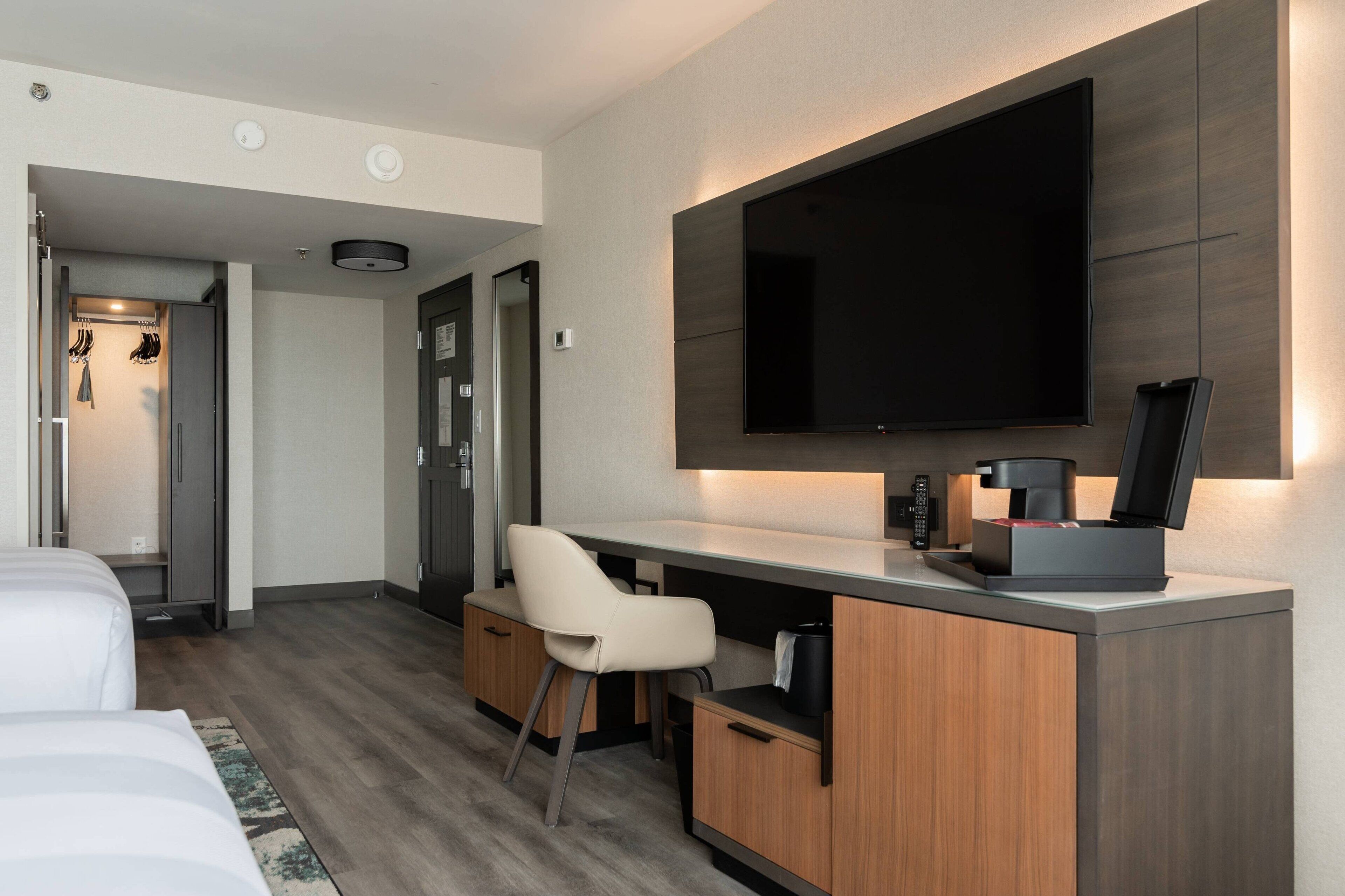 Ein modernes Hotelzimmer mit Bett, Schreibtisch mit Stuhl, Flachbildfernseher an der Wand und einer Kaffeemaschine.