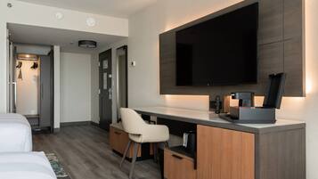 Ein modernes Hotelzimmer mit Bett, Schreibtisch mit Stuhl, Flachbildfernseher an der Wand und einer Kaffeemaschine.