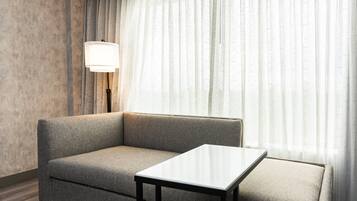 Et moderne hotelværelse med en grå sofa, et lille hvidt bord og en gulvlampe.