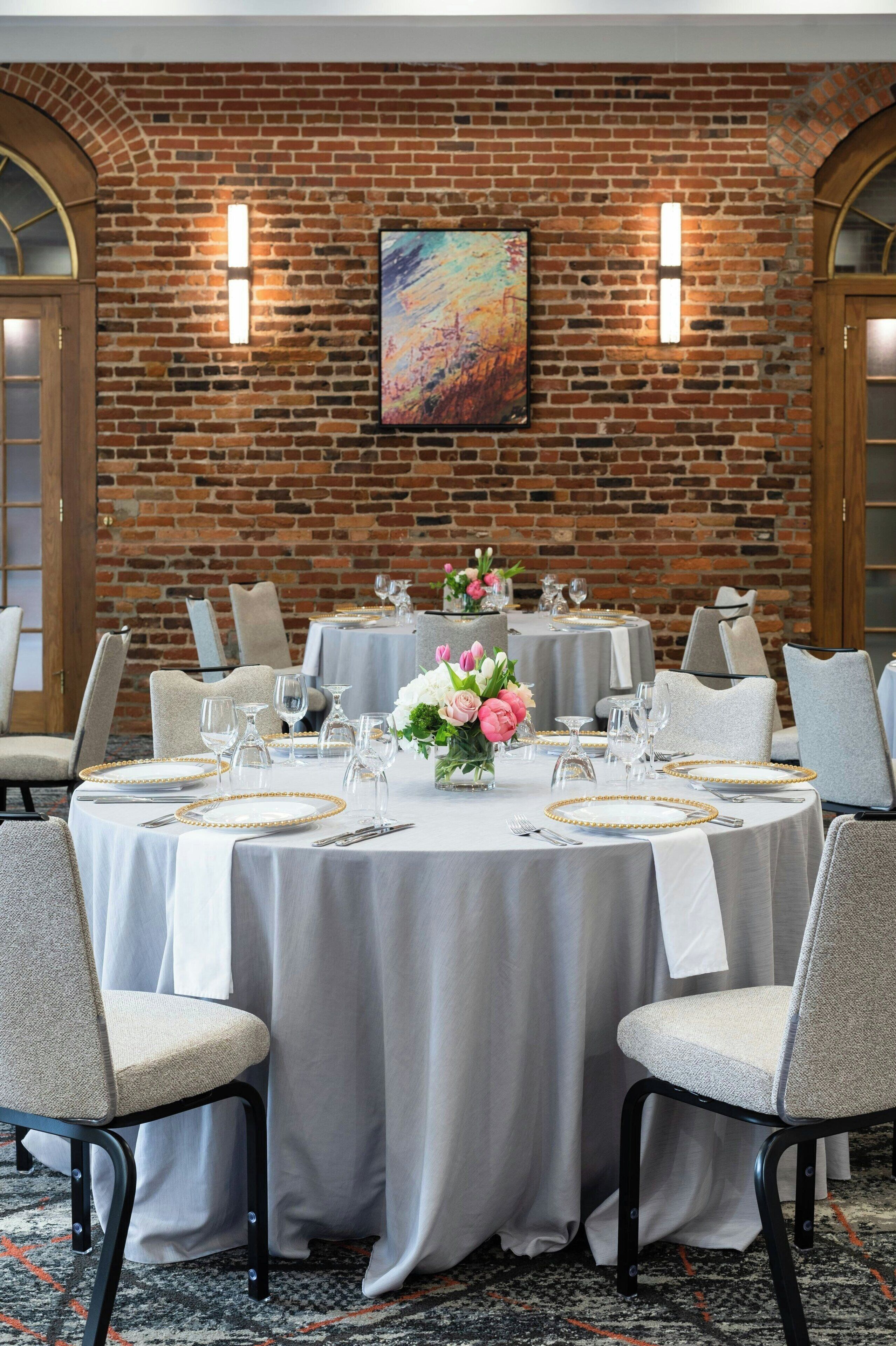 A dining area with round tables, chairs, and a brick wall with two wall-mounted lights.
