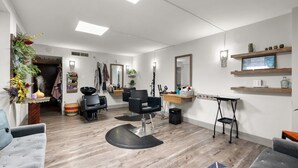 Een moderne kapsalon met een zwarte kappersstoel in het midden, houten vloeren en een spiegel boven een plank met decoratieve objecten.