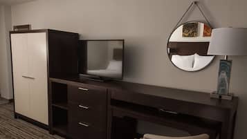 Habitación de hotel con un escritorio de madera oscura, un televisor, un espejo y una lámpara.