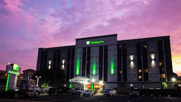 Ein Holiday Inn Hotel mit moderner Fassade, großen Fenstern und einem Parkplatz mit mehreren Fahrzeugen.