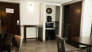 Hotelkamer met een eethoek, een magnetron, een koffiezetapparaat en een spiegel bij de deur.