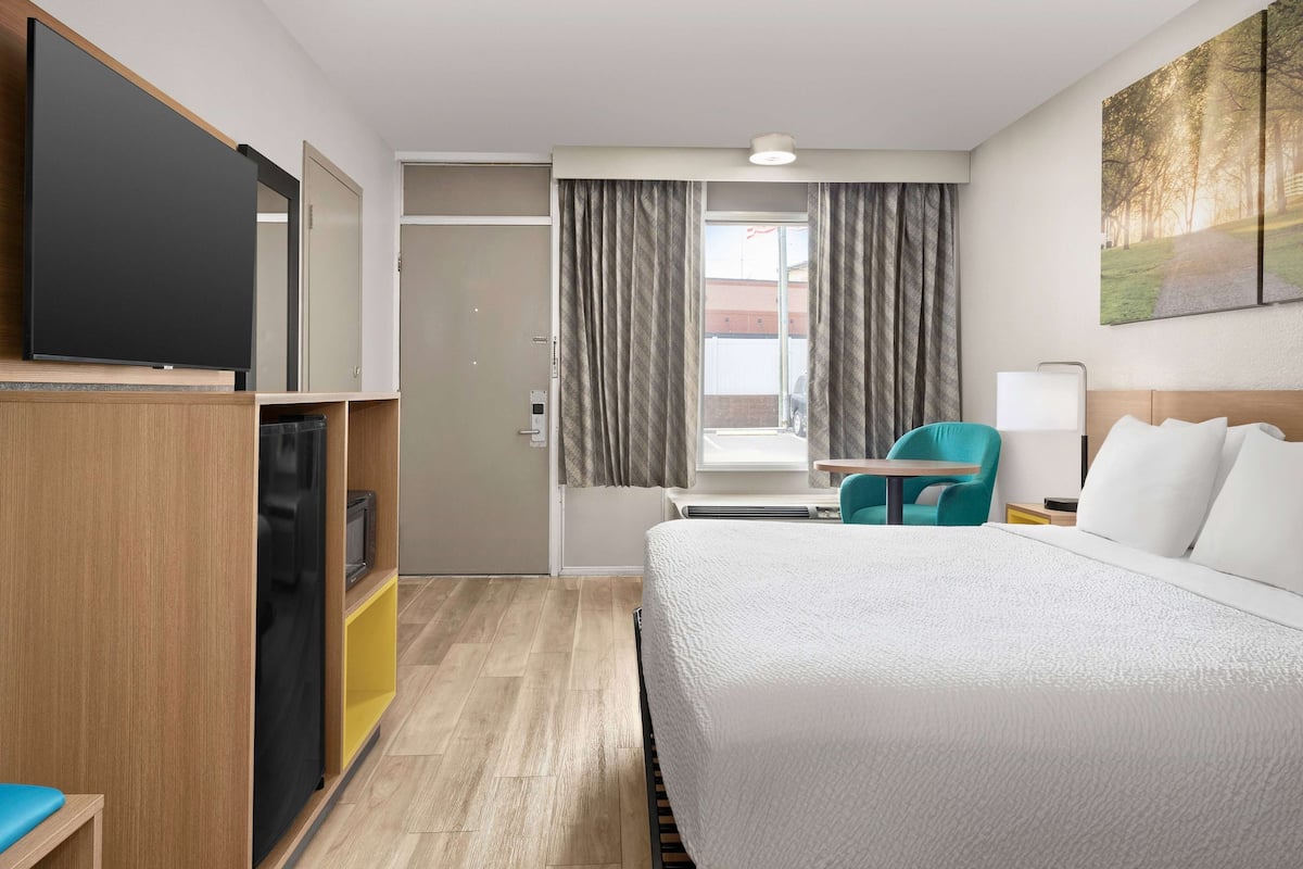 Una habitación de hotel con cama, escritorio, silla, televisor y un cuadro en la pared.