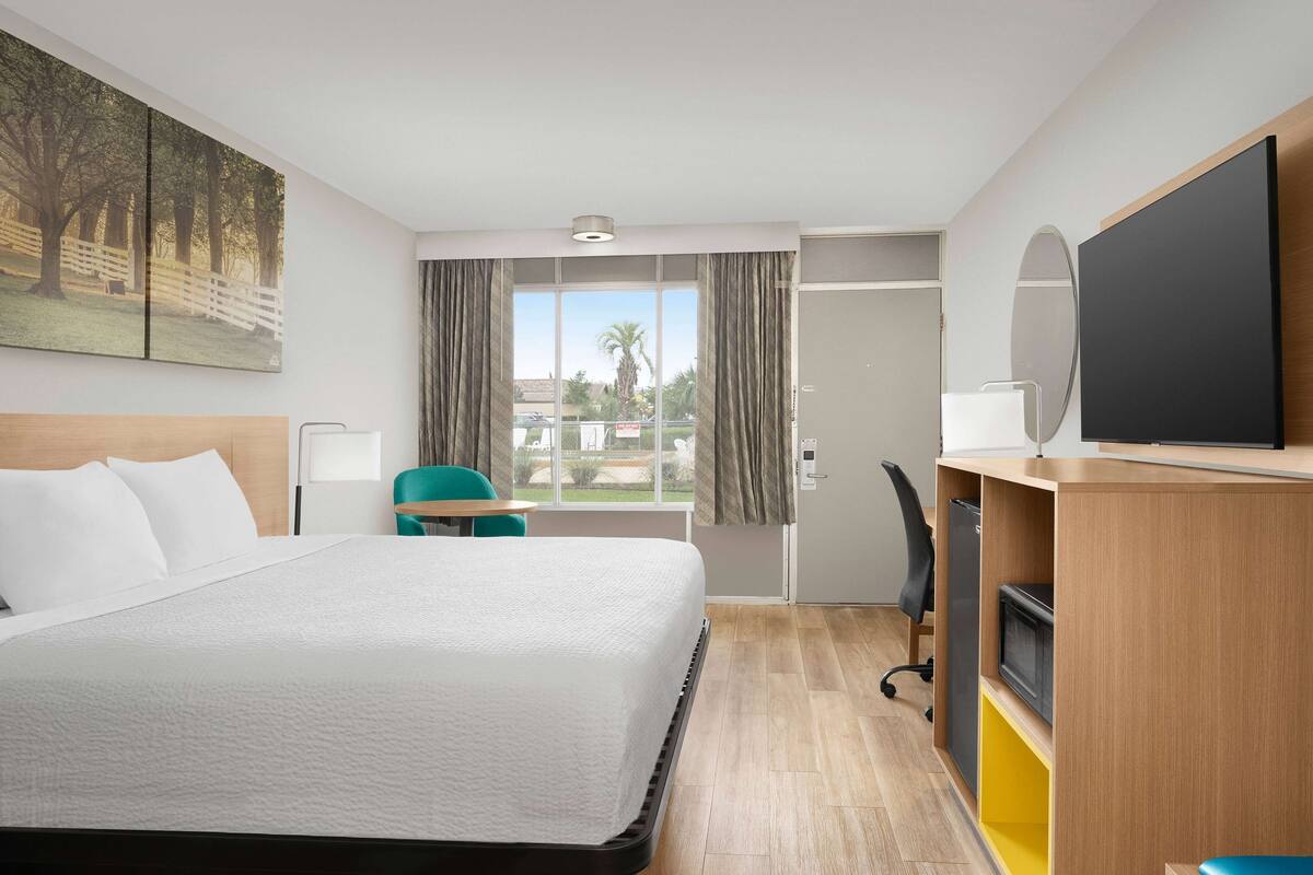 Habitación de hotel con cama, escritorio con computadora, televisor y ventana con cortinas.