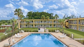 A swimming pool with lounge chairs, a small pool house, and a yellow multi-story building with balconies. - Days Inn by Wyndham Lake City I-75 (Lake City)