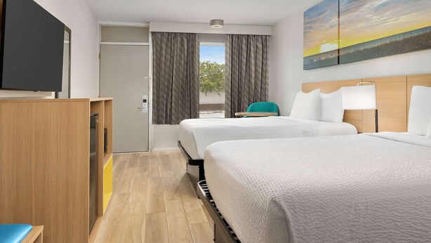 A hotel room with two beds, a TV, a desk, and a painting of a sunset. - Days Inn by Wyndham Lake City I-75 (Lake City)