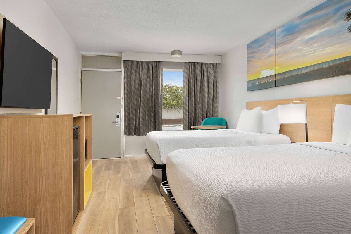 Habitación de hotel con dos camas, televisión, escritorio y un cuadro con un atardecer.
