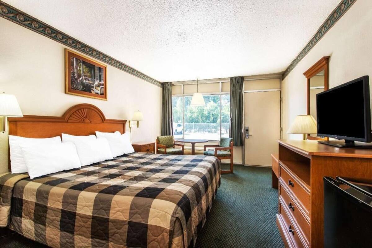Habitación de hotel con cama, televisión, escritorio, silla y ventana con cortinas.