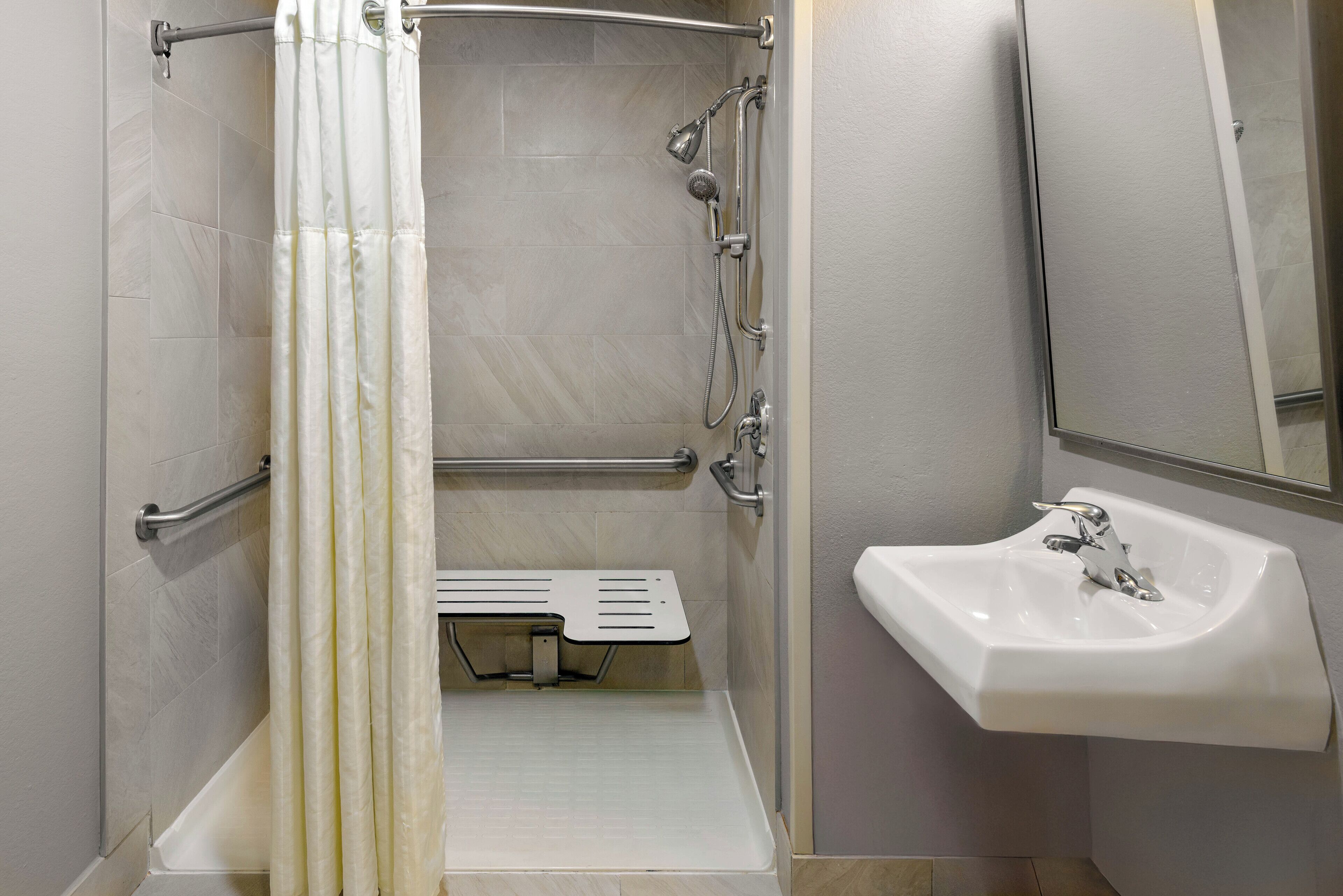 Ein Badezimmer mit Dusche, Haltegriff und Waschbecken.