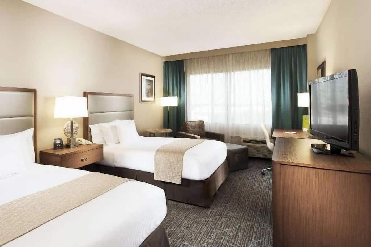 Habitación de hotel con dos camas, televisión, escritorio y ventana con cortinas.
