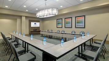 Uma sala de conferência com uma longa mesa, cadeiras, garrafas de água e uma tela de projeção exibindo o logotipo da DoubleTree.