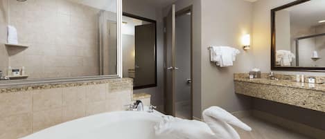 Une salle de bain moderne avec une baignoire, un grand miroir, un meuble-lavabo doté d’un plan de travail en granit et un espace douche.
