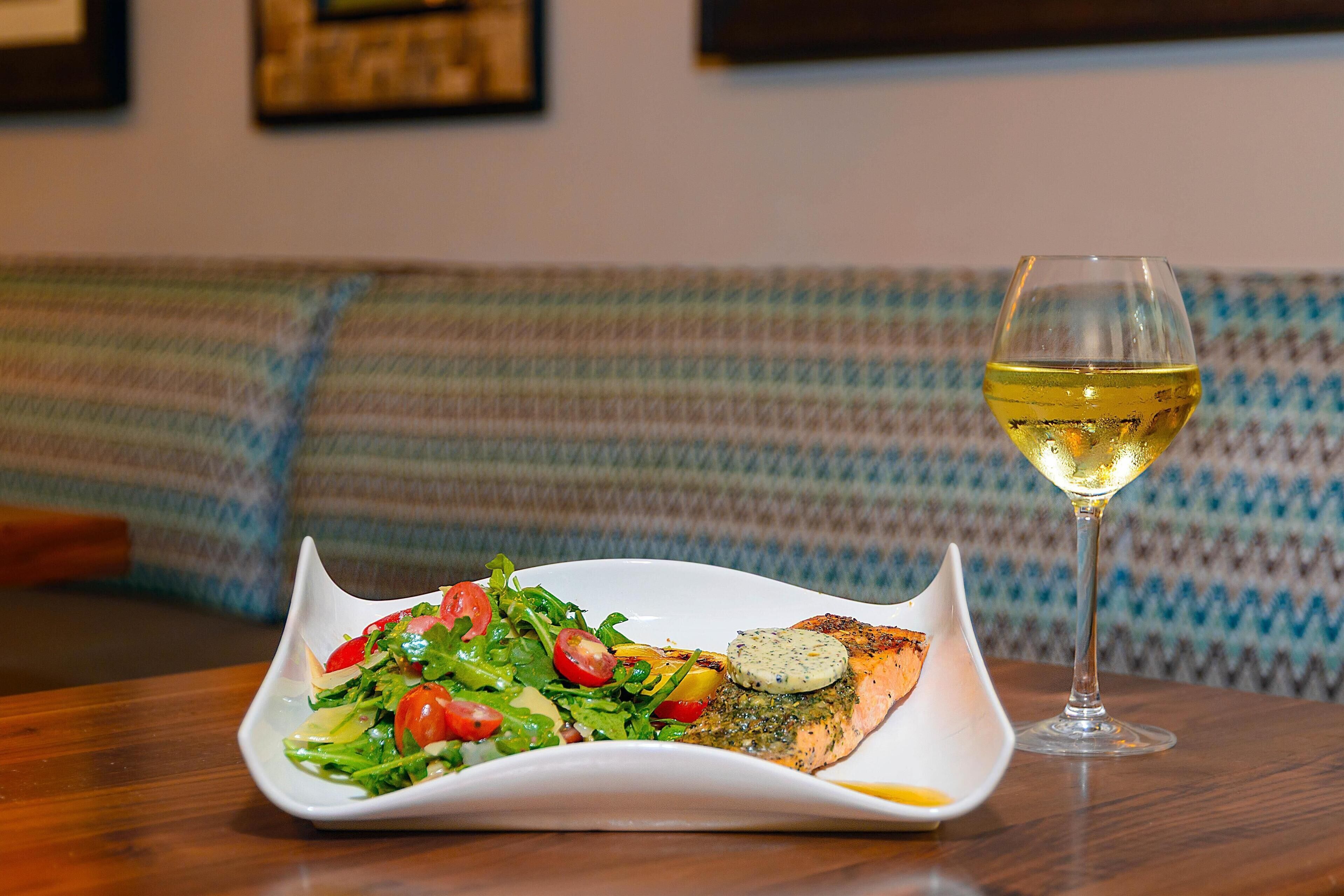 A plate of food with a glass of white wine on a table.