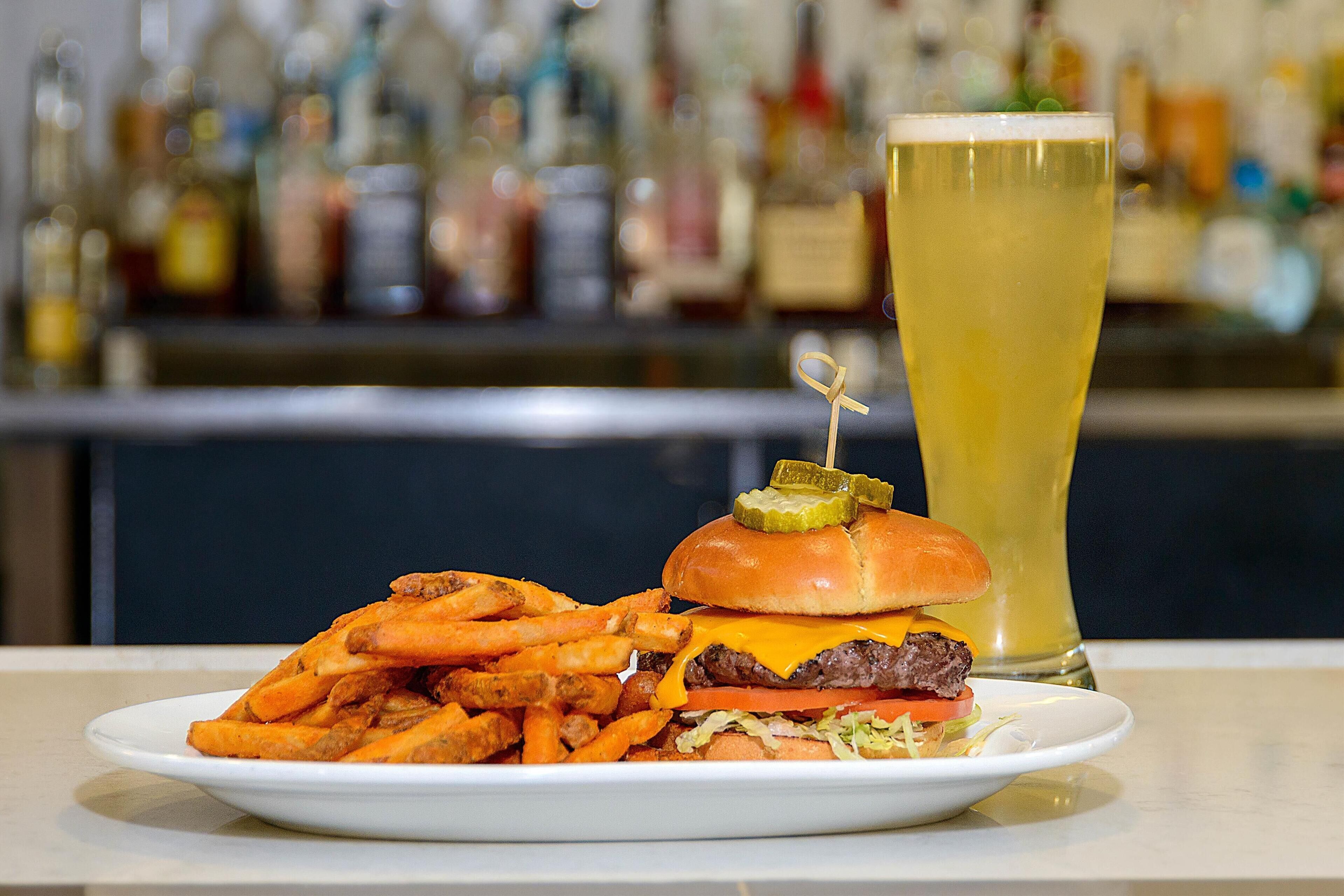 Un plato con una hamburguesa, papas fritas y un vaso alto de cerveza.