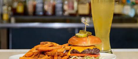 Un plato con una hamburguesa, papas fritas y un vaso alto de cerveza.
