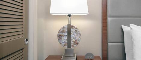 A bedside table with a lamp, a clock, and a bed with a headboard.