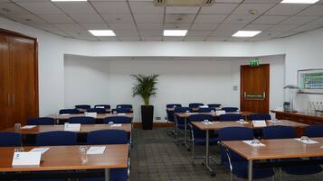 A conference room with tables, chairs, a potted plant, and a push bar to open a door.