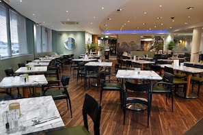 Un restaurante con varias mesas y sillas, suelo de madera y vistas al exterior a través de amplios ventanales.