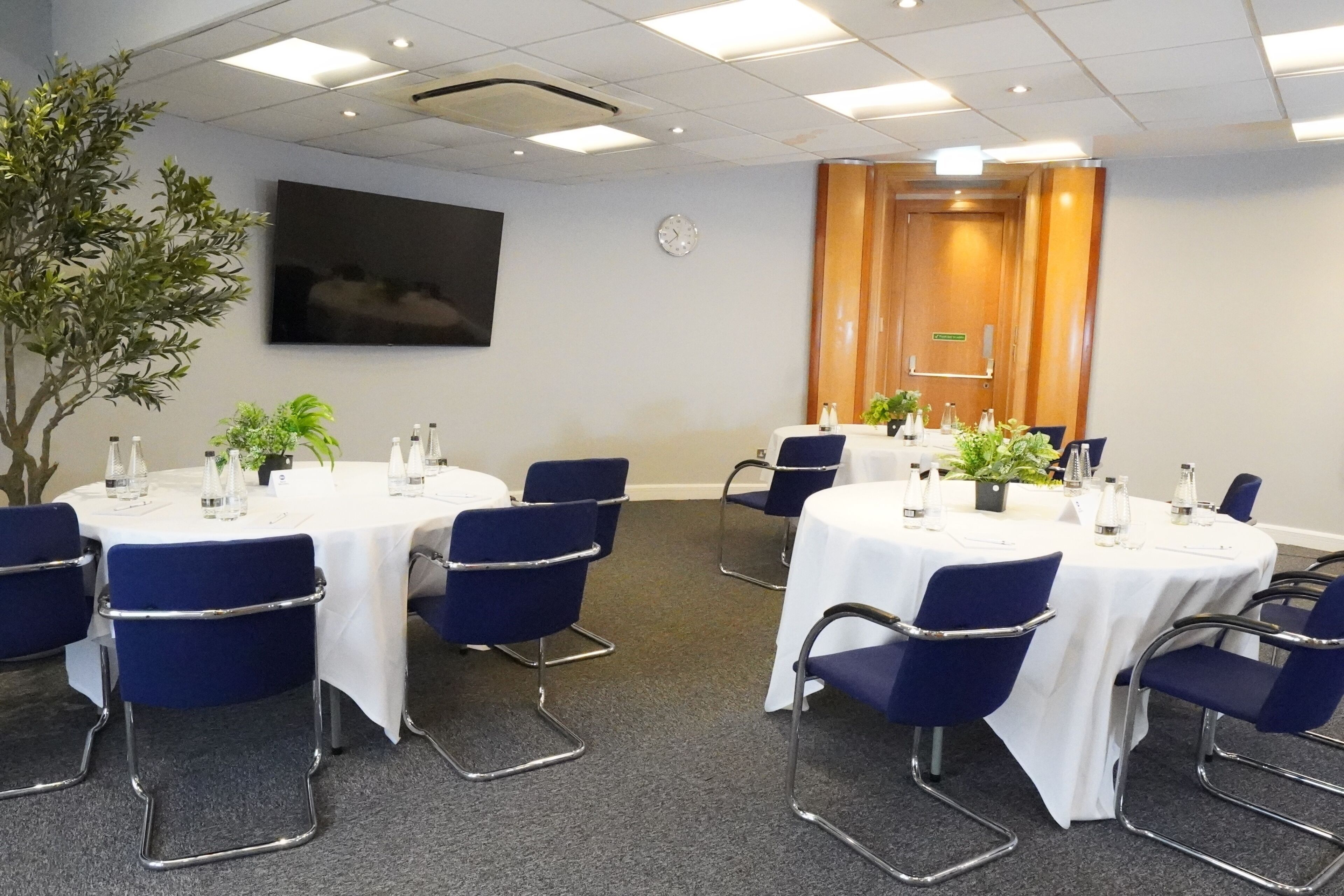 Ett konferensrum med runda bord, blå stolar och krukväxter.