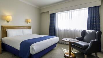 A hotel room with a large bed, a small round table, a leather armchair, and two wall-mounted lamps.