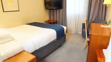 A hotel room with a bed, a desk, a chair, a television, and a framed picture on the wall.