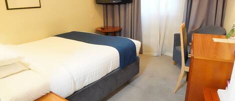 A hotel room with a bed, a desk, a chair, a television, and a framed picture on the wall.