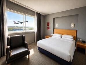 A hotel room with a large bed, a leather armchair, a nightstand, and a window with a view of an airplane. - Best Western Heathrow Ariel T2, 3, 4 (Hayes)